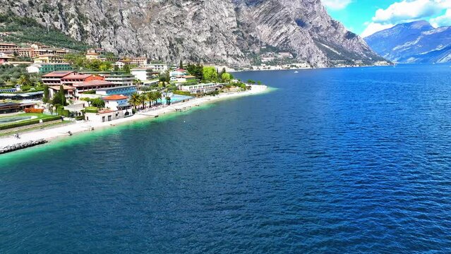 Aerial Panning Shot Of Town Near Lake Garda And Mountain Ranges, Drone Forward Over Beach On Sunny Day - Limone sul Garda, Italy