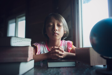 Child girl praying on bible with light in morning at home, christian concept.