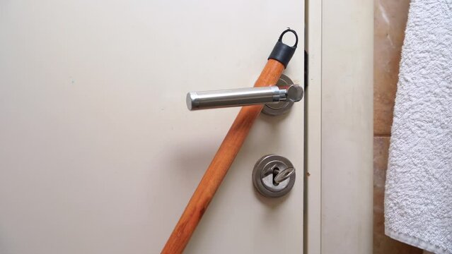 Person trying to enter closed restroom pulling metal door handle. Another person tries to block door handle with stick for mop in bathroom