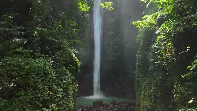 Drone shoot. Waterfall hidden in tropical rainforest jungle,  falling water hitting water surface, some huge rocks seeable in through splashes. Lush green leaves is moving from the wind. Philippines