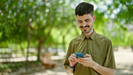 Fototapeta premium Young hispanic man using smartphone smiling at park