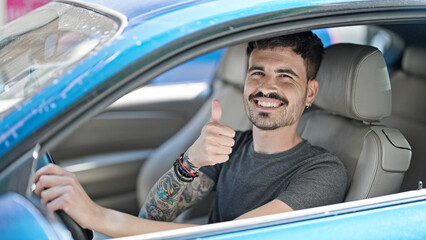 Young hispanic man driving car doing ok gesture with thumb up at street