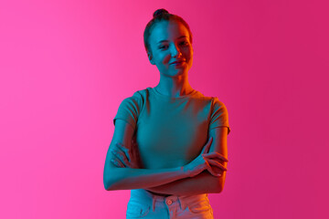 Beautiful young girl with hairbun, smiling, looking tenderly at camera against pink studio background in neon light. Concept of human emotions, fashion, beauty, lifestyle, youth, ad © master1305