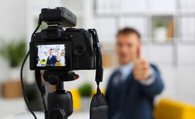 Male in suit and tie show confirm sign arm making promo videoblog or photo session in office camcorder to tripod closeup. Vlogger promotion selfie solution or finance advisor management information