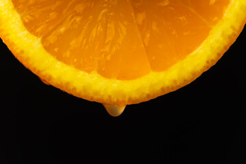 Macro photography, a drop of juice dripping from a slice of orange on a black background. Fruit background