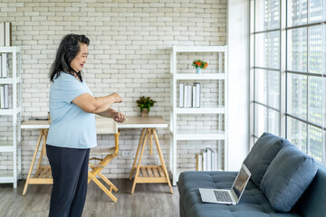 Elderly asian woman watching video tutorial doing stretching fitness exercise yoga. Elderly women training online courses on laptop while exercising in living room. Workout training online concept