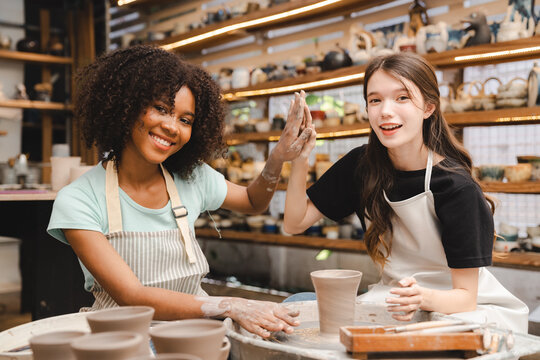 The potter's hands are gently and surely formed by a clay pot on a potter's wheel. The master potter works in a workshop, Woman hands working on pottery wheel making a clay pot, raw clay shaping