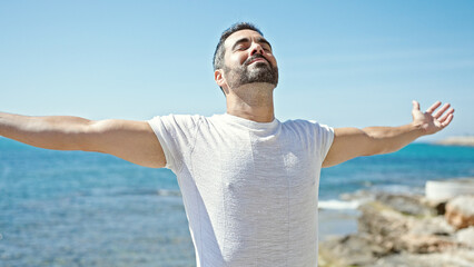 Young hispanic man breathing with closed eyes and arms open at the beach - Powered by Adobe