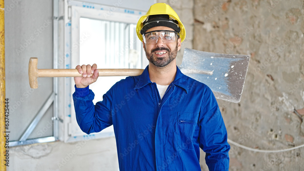 Canvas Prints Young hispanic man worker wearing hardhat holding shovel at construction site