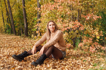 A beautiful young woman sitting in a forest on a dry autumn leaves.