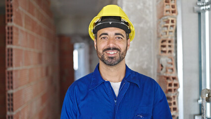 Young hispanic man worker wearing hardhat taking glasses off at construction site