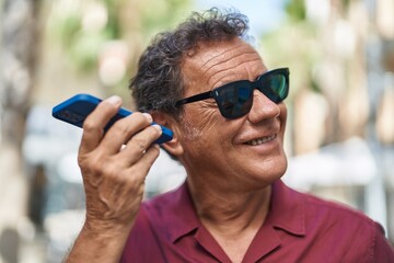 Middle age man smiling confident listening audio message by the smartphone at street