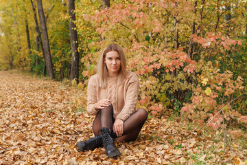 A beautiful young woman sitting in a forest on a dry autumn leaves.