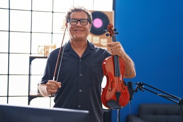 Middle age man musician smiling confident holding violin at music studio