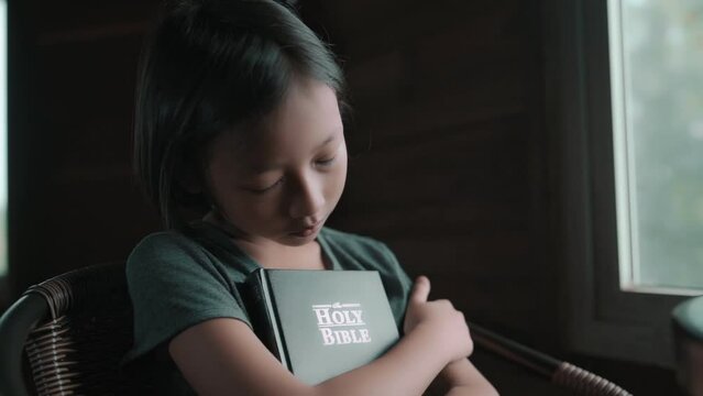 Child girl hugging the bible and sleeping in chair, christian concept. High quality 4k video.