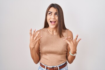 Young hispanic woman standing over white background crazy and mad shouting and yelling with...