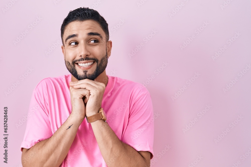 Wall mural hispanic young man standing over pink background laughing nervous and excited with hands on chin loo