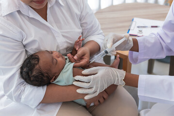 Obraz na płótnie Canvas The doctor is vaccinating prevent virus for 1-month-old baby newborn son is half Thai half Nigerian, who is lying on mother's lap, to vaccine for baby and health care concept.