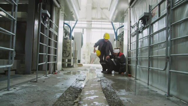 Wide shot of female worker taking first aid kit and helping injured male colleague with bandaged head to stand up and walk away after accident at industrial factory