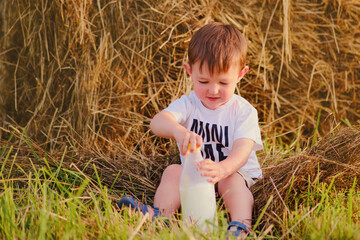 Naklejka na ściany i meble With the autumn sun, the child gleefully plays on the farm, surrounded by hay stacks and the beauty of nature. Portrait of a happy kid aged two years