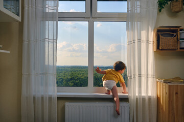 The little baby is dangerously climbing up the window sill, oblivious to the hazard. Kid aged two years
