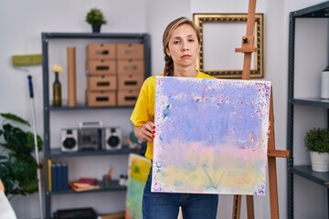 Young blonde woman holding canvas depressed and worry for distress, crying angry and afraid. sad...