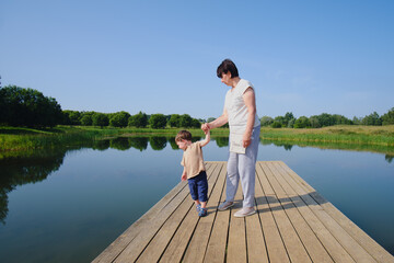 Fototapeta na wymiar A real joy for a baby is a walk with his grandmother on the pier. The family is happily strolling along the wooden pier on the lake. Kid aged two years