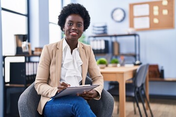 Young african american woman business worker writing on paperwork sitting on chair at office