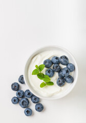 Top view of yogurt with ripe blueberries and mint in a white bowl and scattered with copy space