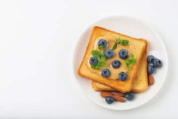 Toast with almond butter, blueberries and fresh mint on white plate with copy spase. Sandwich with berries and nuts for breakfast top view