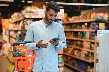 Young man using mobile phone while shopping at supermarket