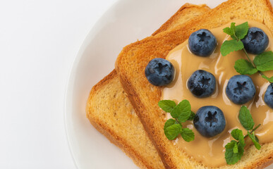 Toast with peanut butter, blueberries and fresh mint on white plate. Sandwich with berries for breakfast top view  clouse up