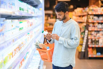 Portrait of handsome young Indian man standing at grocery shop or supermarket, Closeup. Selective...