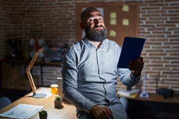 Young hispanic man with beard and tattoos working at the office at night puffing cheeks with funny face. mouth inflated with air, crazy expression. - obrazy, fototapety, plakaty