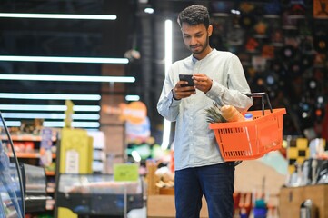 Young man using mobile phone while shopping at supermarket