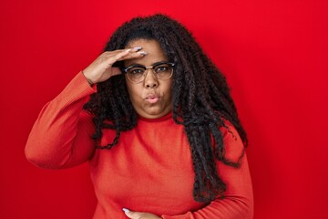 Plus size hispanic woman standing over red background worried and stressed about a problem with...