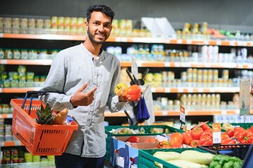 Closeup portrait, handsome young man picking up bell peppers, choosing yellow and orange vegetables in grocery store