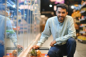 Portrait of handsome young Indian man standing at grocery shop or supermarket, Closeup. Selective Focus.
