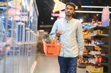 Portrait of happy Indian man standing in front of the product counter in a grocery store. Man buying grocery for home in supermarket.