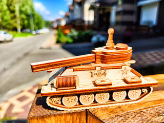 Wooden toy tank with Russian inscription t-34 and city or village houses on sunny day. War between...