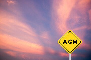 Yellow transportation sign with word AGM (Abbreviation of annual general meeting) on violet color sky background