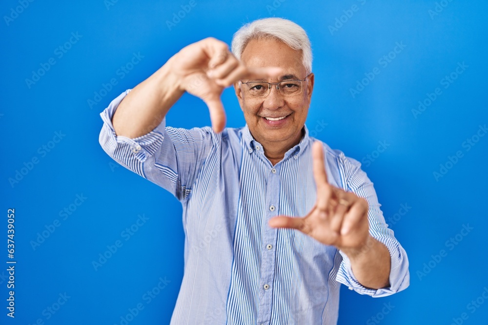 Sticker hispanic senior man wearing glasses smiling making frame with hands and fingers with happy face. cre