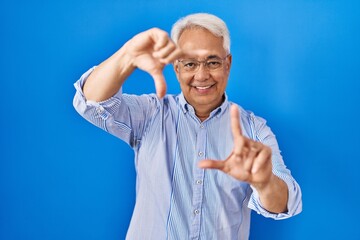 Fototapeta premium Hispanic senior man wearing glasses smiling making frame with hands and fingers with happy face. creativity and photography concept.