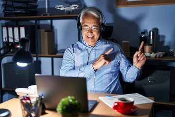 Fototapeta na wymiar Hispanic senior man wearing call center agent headset at night smiling and looking at the camera pointing with two hands and fingers to the side.