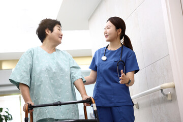 병원 복도에서 보조기를 이용하여 걸어가는 환자와 간호사가 서로 마주보며 웃으며 격려하는 모습 