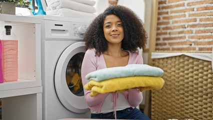 African american woman washing clothes holding folded towels at laundry room