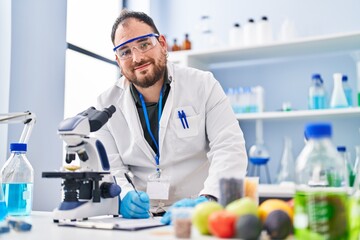 Young hispanic man scientist write on report using microscope at laboratory