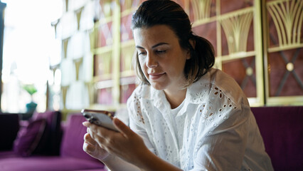 Beautiful young hispanic woman using smartphone at hotel hall