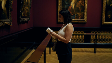 Young beautiful hispanic woman visiting art gallery reading brochure at Art Museum in Vienna