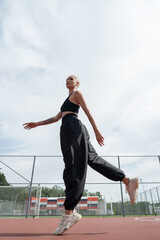 Fototapeta na wymiar A blonde woman with a short haircut shows her agility and fitness as she jumps on a running track. She wears a black outfit and white sneakers
